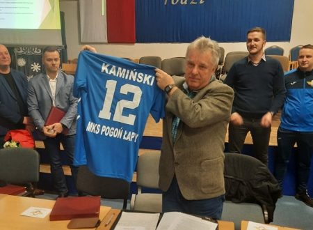 Prezes klubu Pogoń Łapy trzyma koszulkę klubową. Z tyłu stoją zawodnicy Pogoni Łapy