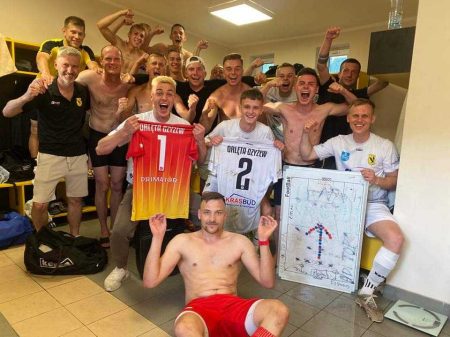 Drużyna piłkarska w szatni po meczu cieszy się z wygranej i krzyczy pozując do zdjęcia. Napinają muskuły. Piłkarze Orląt Czyżew