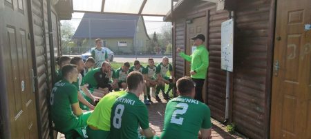 piłkarze LZS-u Krynki słuchają, co mówi ich trener. Zebrani sa w okręgu, siedząc, a trener stoi. Za trenerem jest tablica.